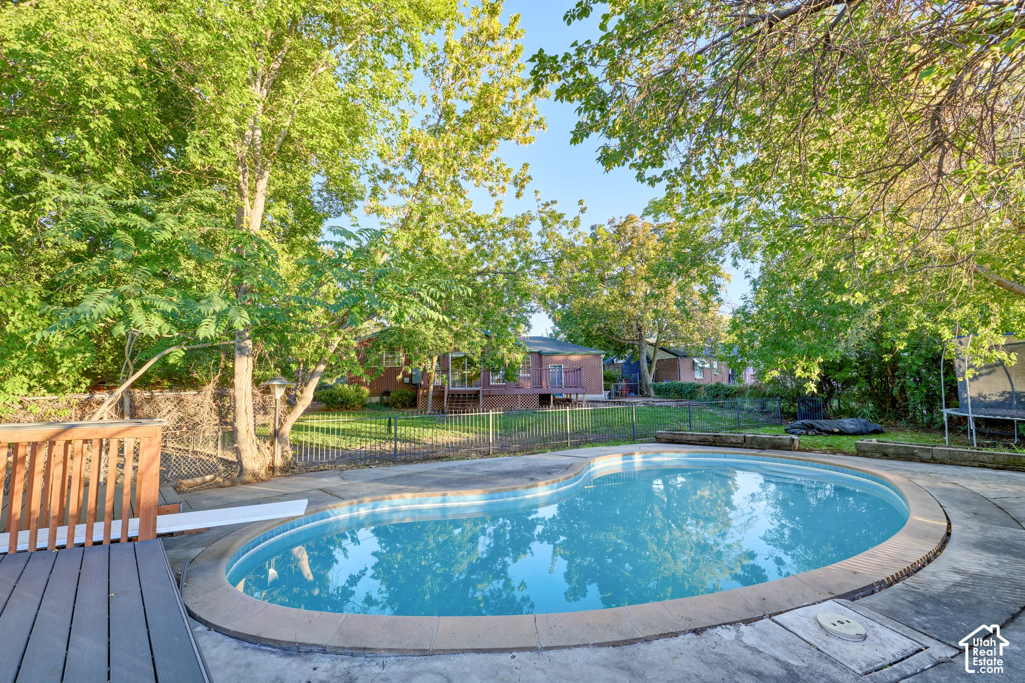 Freeform swimming pool with a diving board, surrounded by concrete decking and mature trees