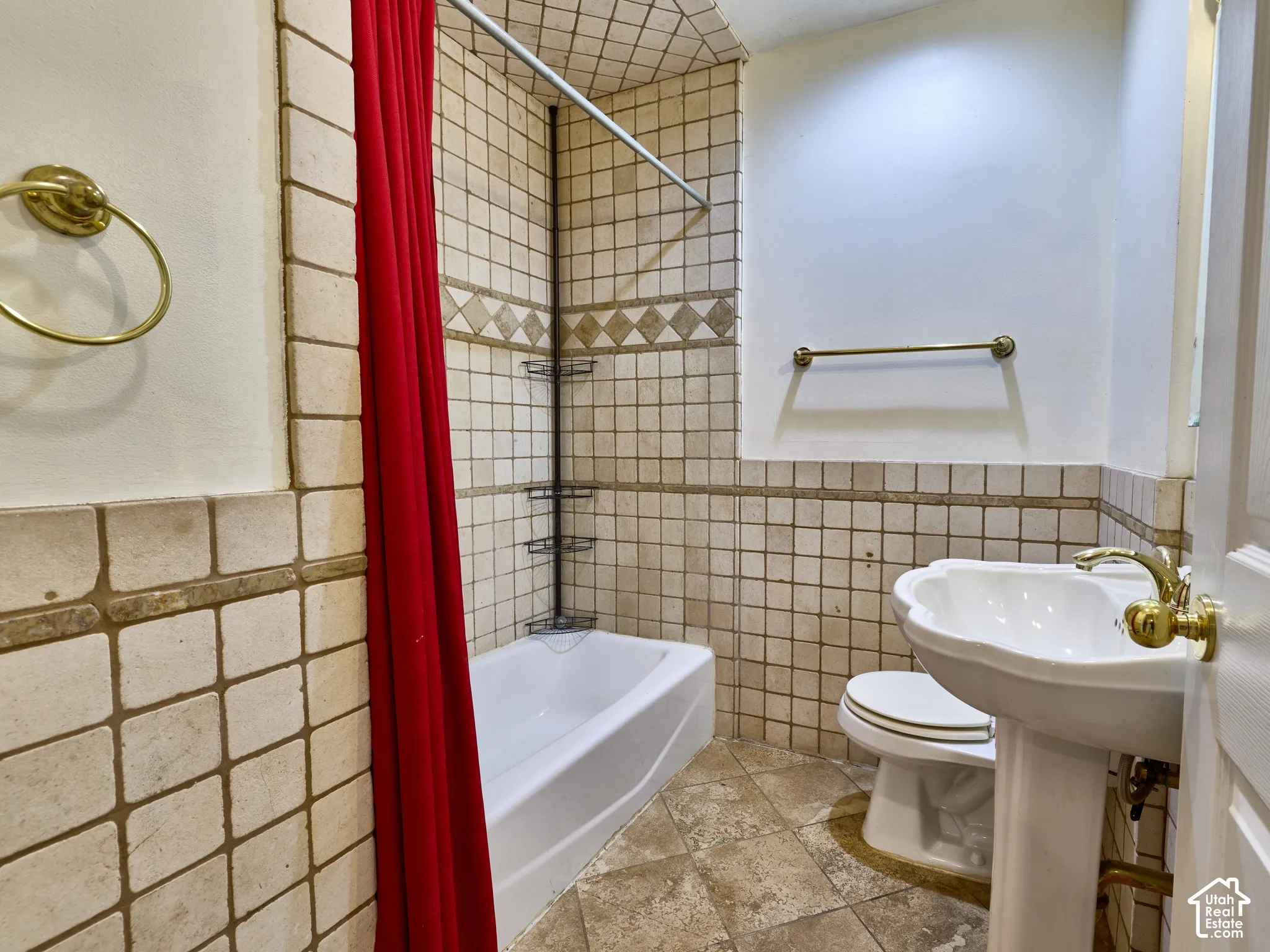 Bathroom featuring a pedestal sink with brass-finish fixtures, white bathtub, wall-mounted towel bar, and floor-to-ceiling tile