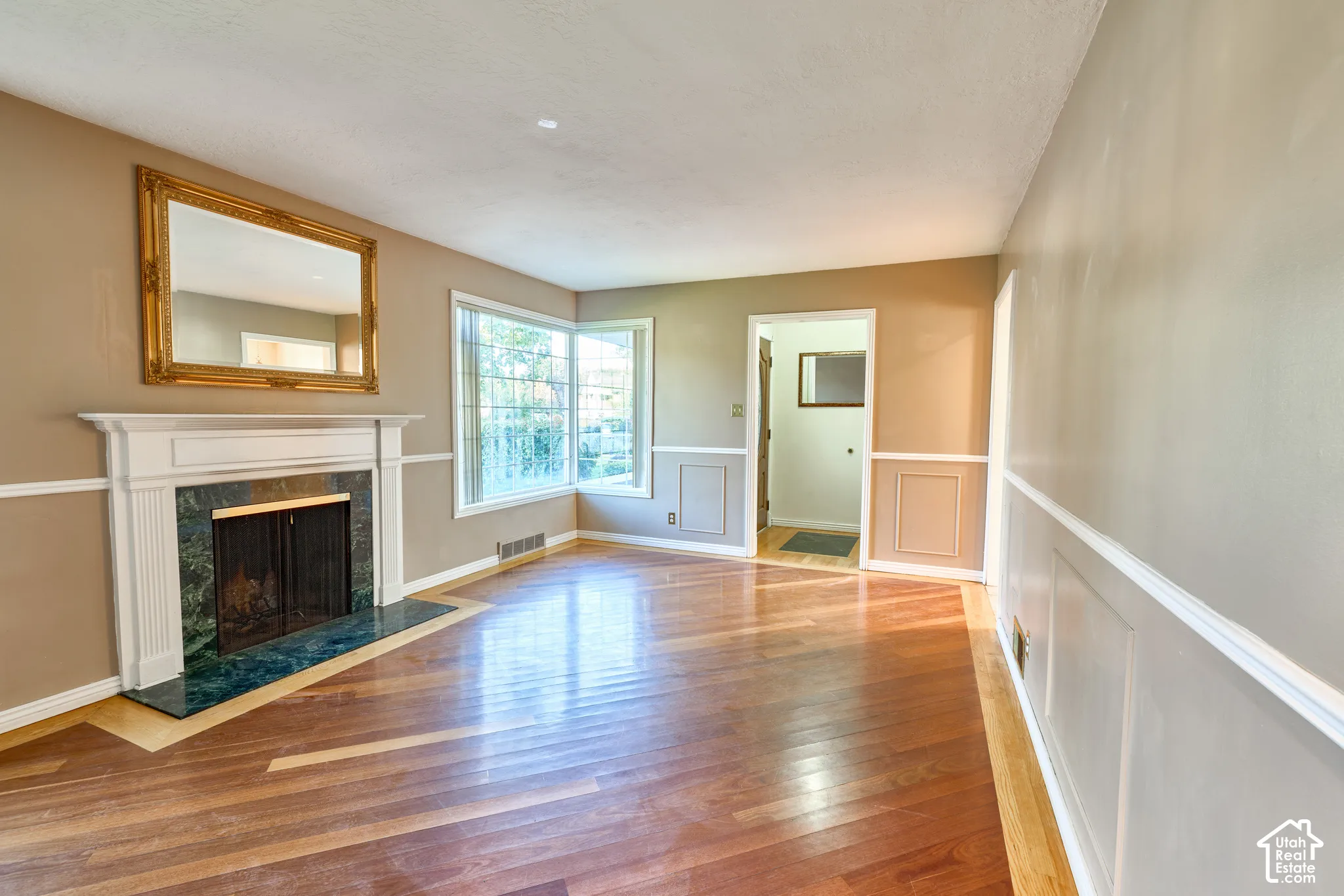 Hardwood flooring with inlay detail, white wainscoting, white mantel fireplace with a green marble surround, and multiple windows