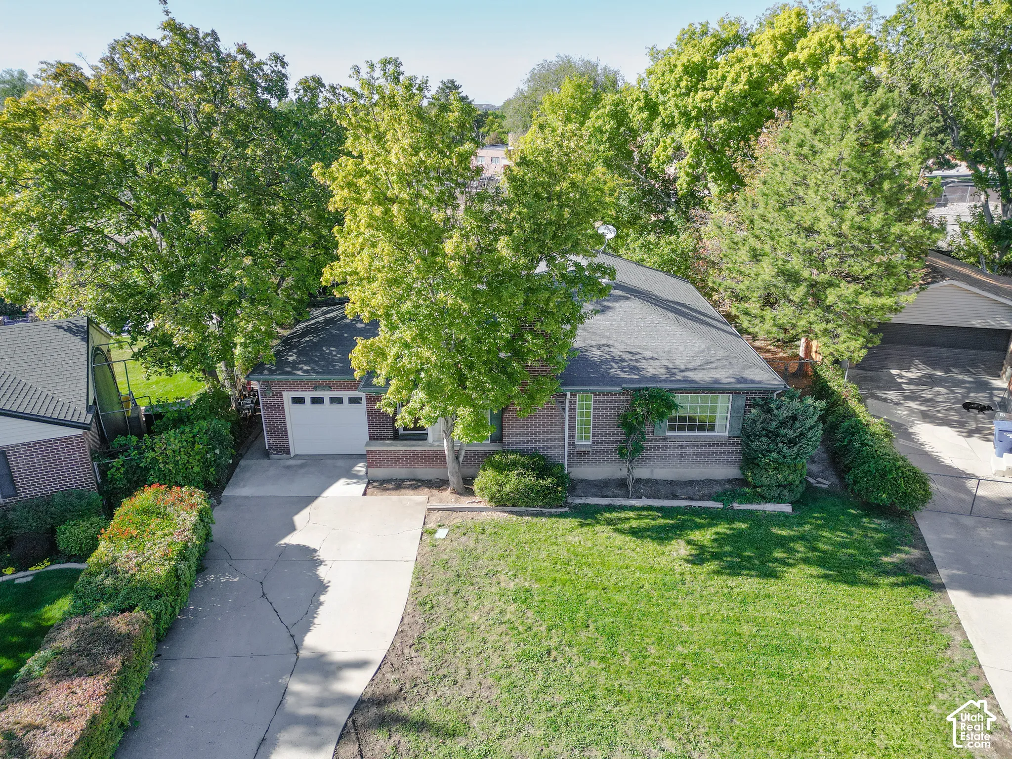 Brick exterior, attached garage, shingle roof, concrete driveway, and established landscaping