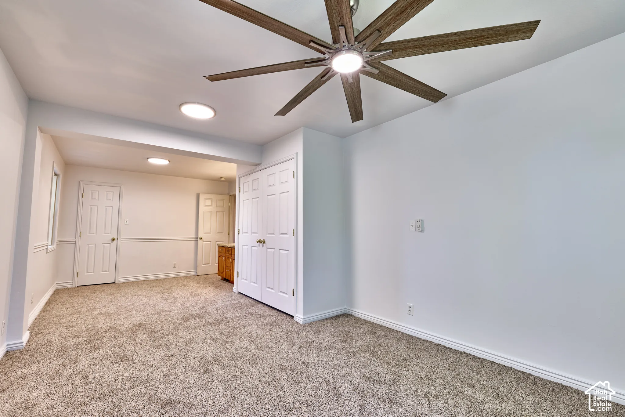 Neutral-toned carpet flooring, a multi-blade ceiling fan with integrated lighting, white paneled doors, and circular recessed lighting fixtures
