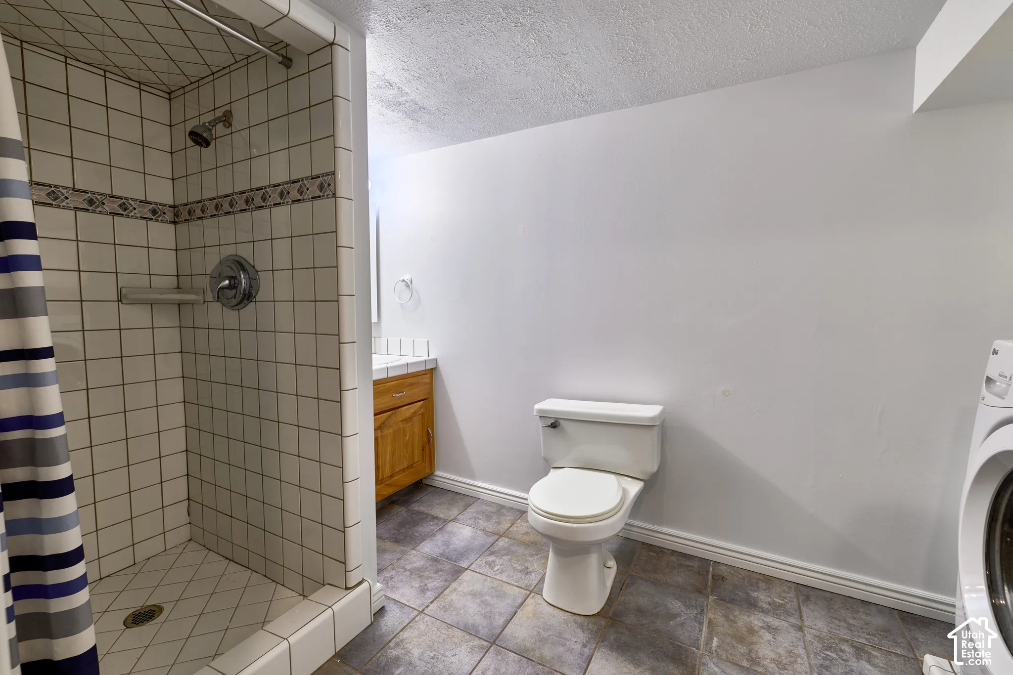 Tile shower with decorative border, wood-finish vanity with tile countertop, and a white toilet