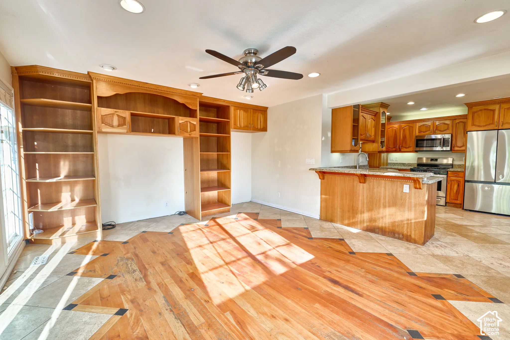 Wood-finish flooring with tile accents, built-in shelving, recessed lighting, ceiling fan, and a kitchen featuring wood cabinetry and stainless steel appliances