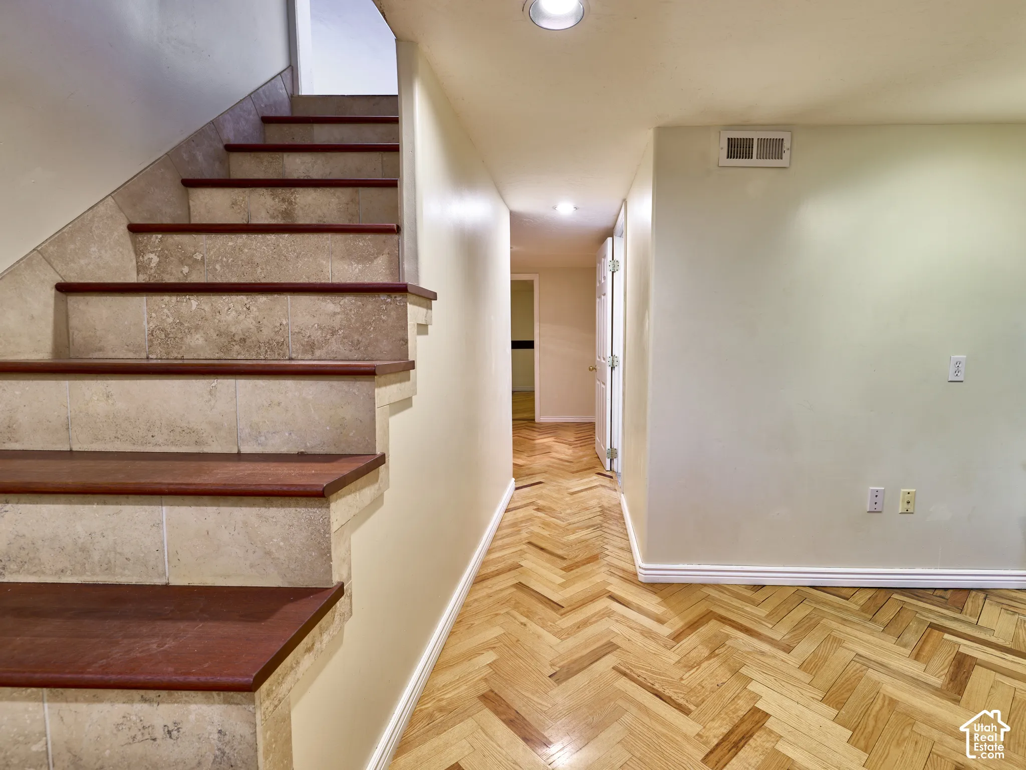 Wood-finish flooring in a herringbone pattern, stone-clad staircase with wood-finish treads, recessed ceiling lighting