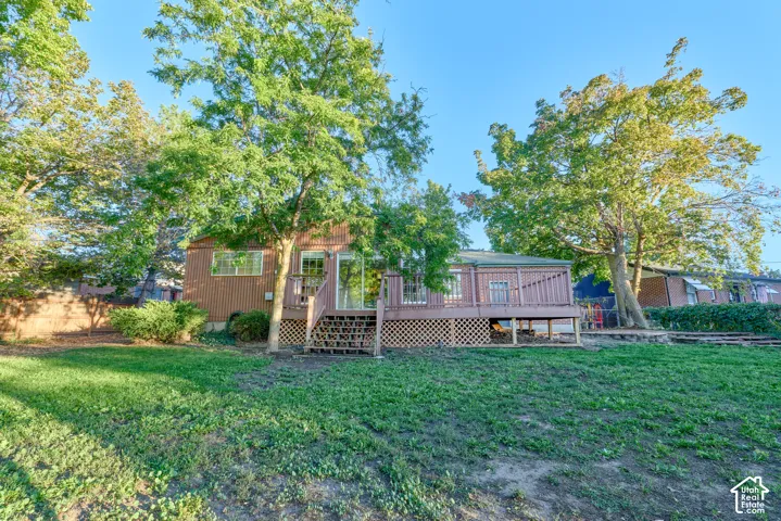 Expansive green lawn with mature trees and a multi-level wooden deck featuring lattice skirting, a sliding glass door, and exterior steps
