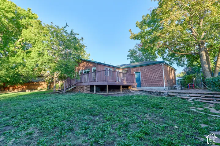 Expansive backyard featuring a large elevated wood deck with railing, exterior brick facade, and mature trees