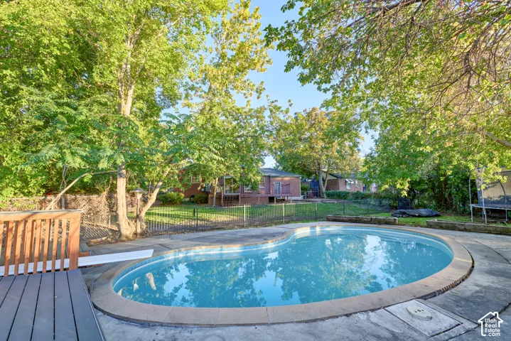 Freeform swimming pool with a diving board, surrounded by concrete decking and mature trees
