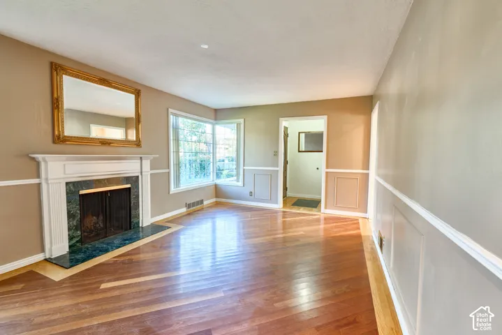 Hardwood flooring with inlay detail, white wainscoting, white mantel fireplace with a green marble surround, and multiple windows