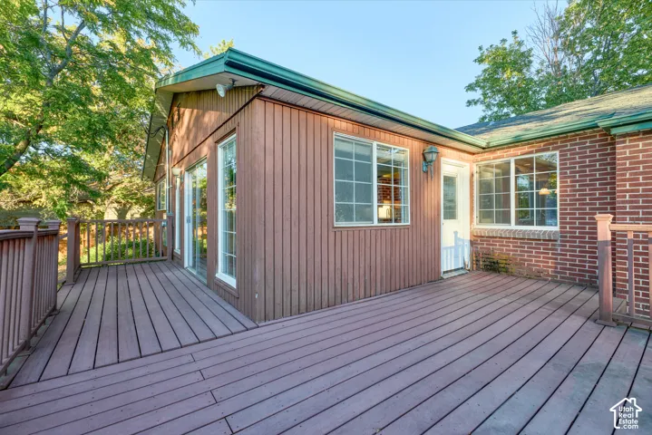 Expansive outdoor deck with railing, featuring a sliding glass door and multiple windows, alongside a brick exterior wall
