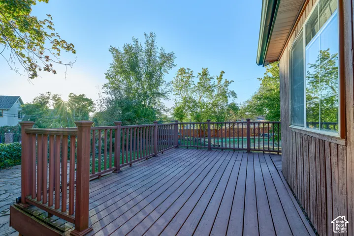 Expansive wood-finish deck with a full railing, vertical siding exterior, and large window