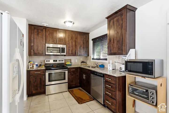 Dark wood cabinetry, stainless steel range, built-in microwave, light-toned tile flooring, and granite countertops