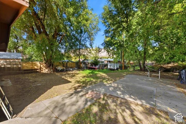 Spacious outdoor area featuring mature trees, a concrete patio, and a grassy lawn