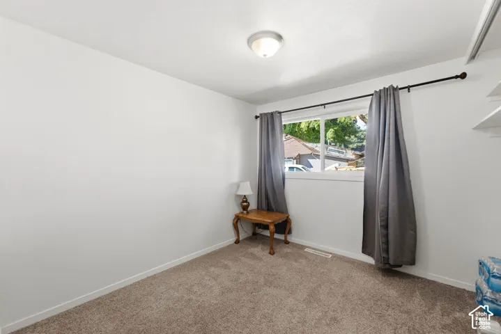 Bright secondary bedroom featuring neutral wall finishes, carpet flooring, and a large window with gray curtain panels and rod