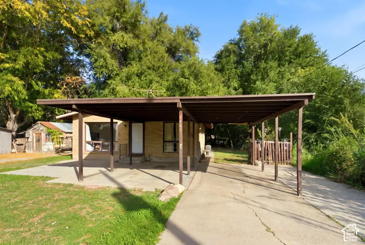Carport with an extended concrete driveway, brick exterior, and mature trees