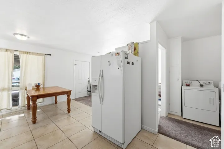 Spacious kitchen featuring white side-by-side refrigerator with ice and water dispensers, ceramic tile flooring, and dedicated laundry area with front-load washer and electric dryer