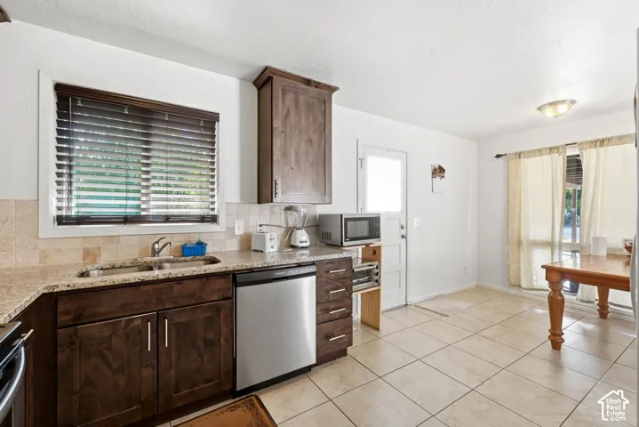 Kitchen featuring wood-finish cabinetry, granite-style countertops, stainless steel dishwasher, and tiled flooring