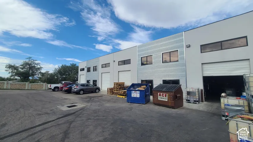 Commercial building with multiple roll-up garage doors, a paved parking area, and upper-level windows