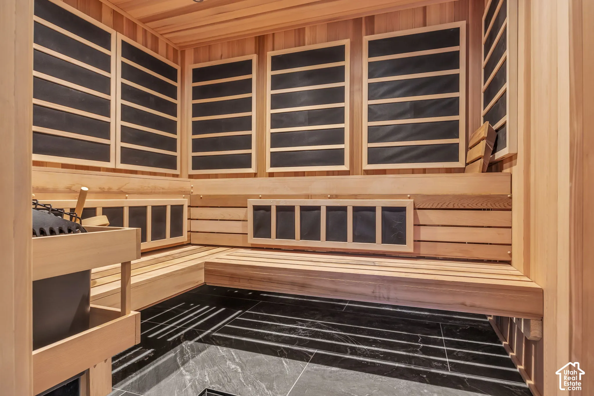 Cedar-lined sauna with tiered wood benches, dark-toned wall panels, and dark-toned floor tiling