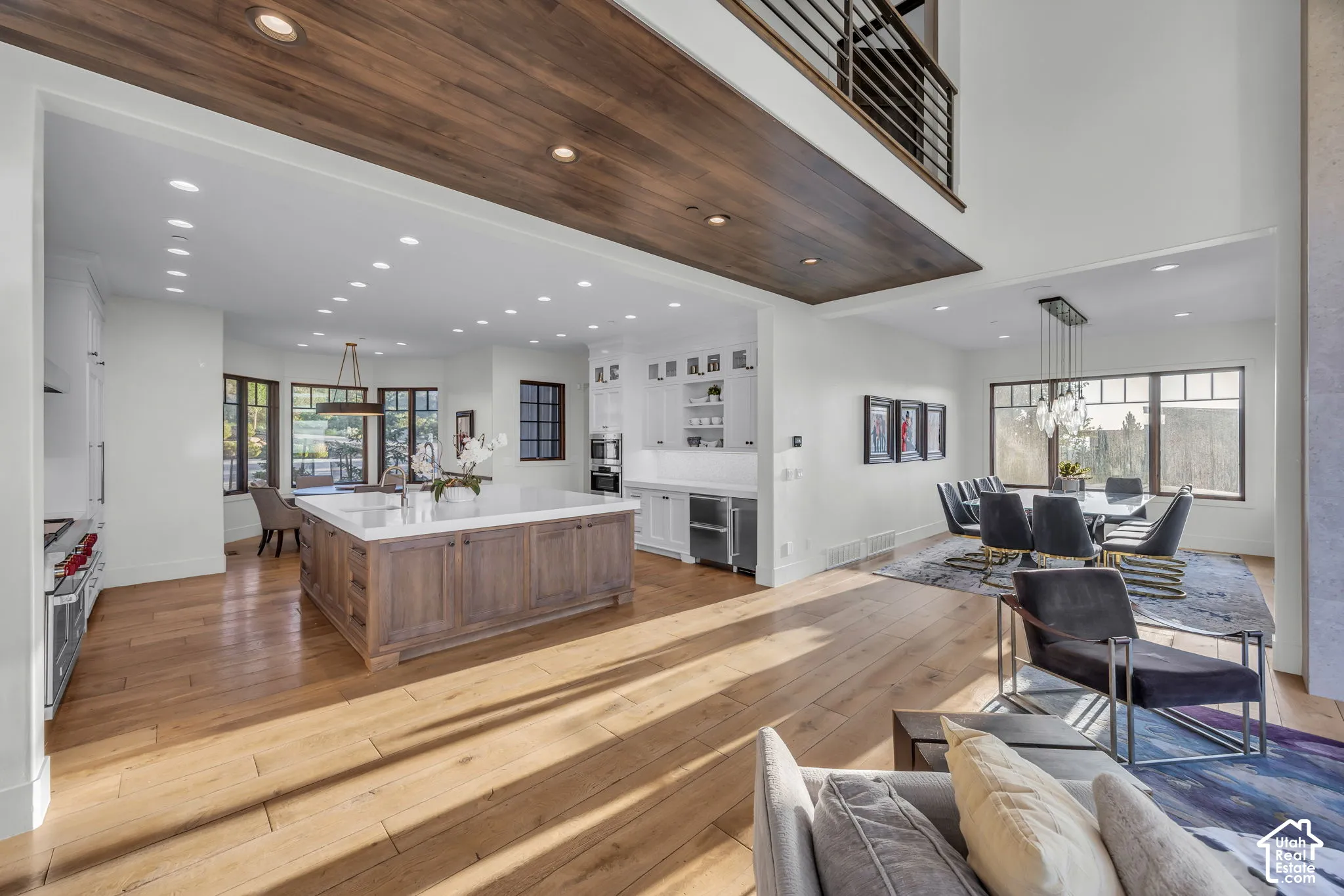 Expansive living area with wood-finish flooring, a kitchen island with stone countertop, white built-in cabinetry, and a dining area with large windows