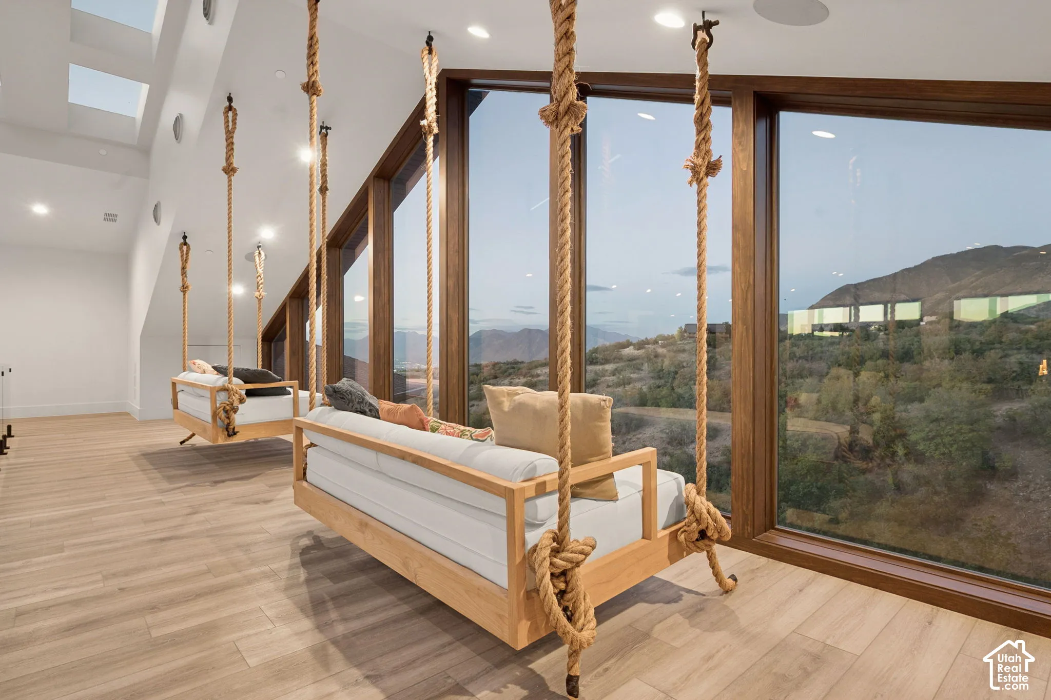 Expansive full-height windows with mountain scenery, natural wood-finish flooring, recessed lighting, and skylights