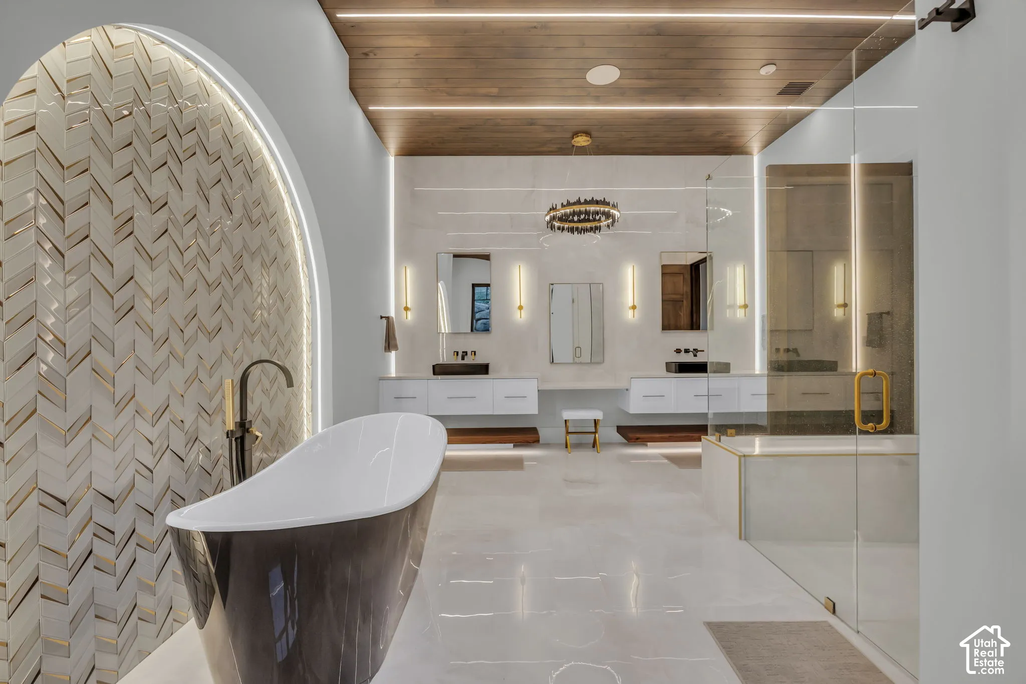 Freestanding soaking tub, arched chevron-patterned tile wall, dual floating vanities with vessel sinks, walk-in glass-enclosed shower, and wood-finish ceiling