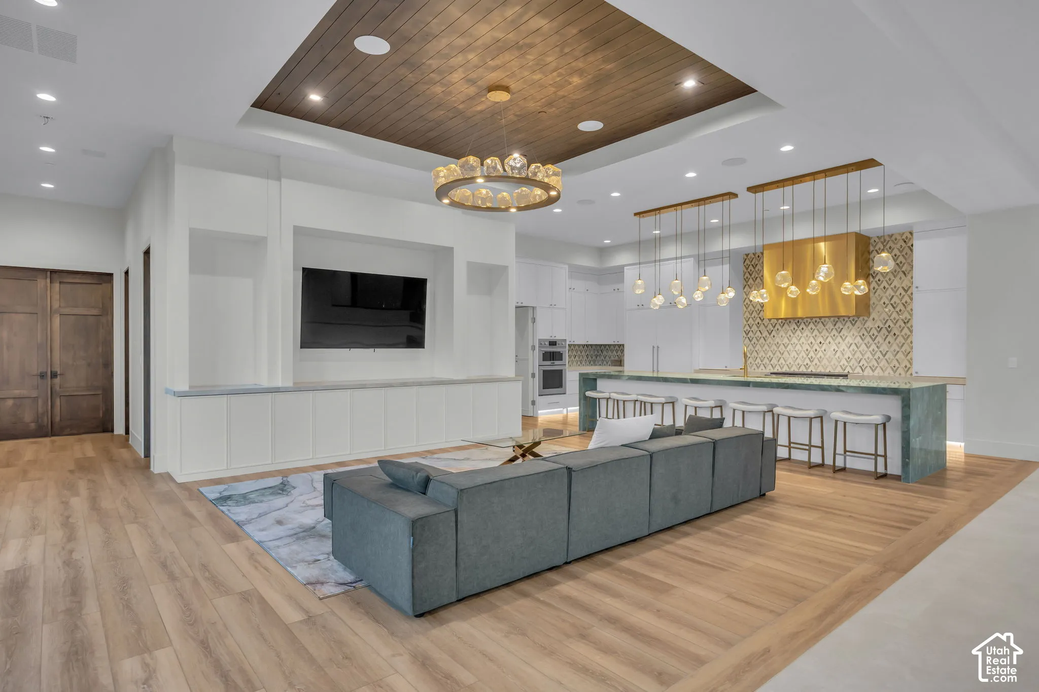 Wood-finish flooring throughout, tray ceiling with wood paneling, built-in media center, kitchen island with seating, and custom pendant lighting
