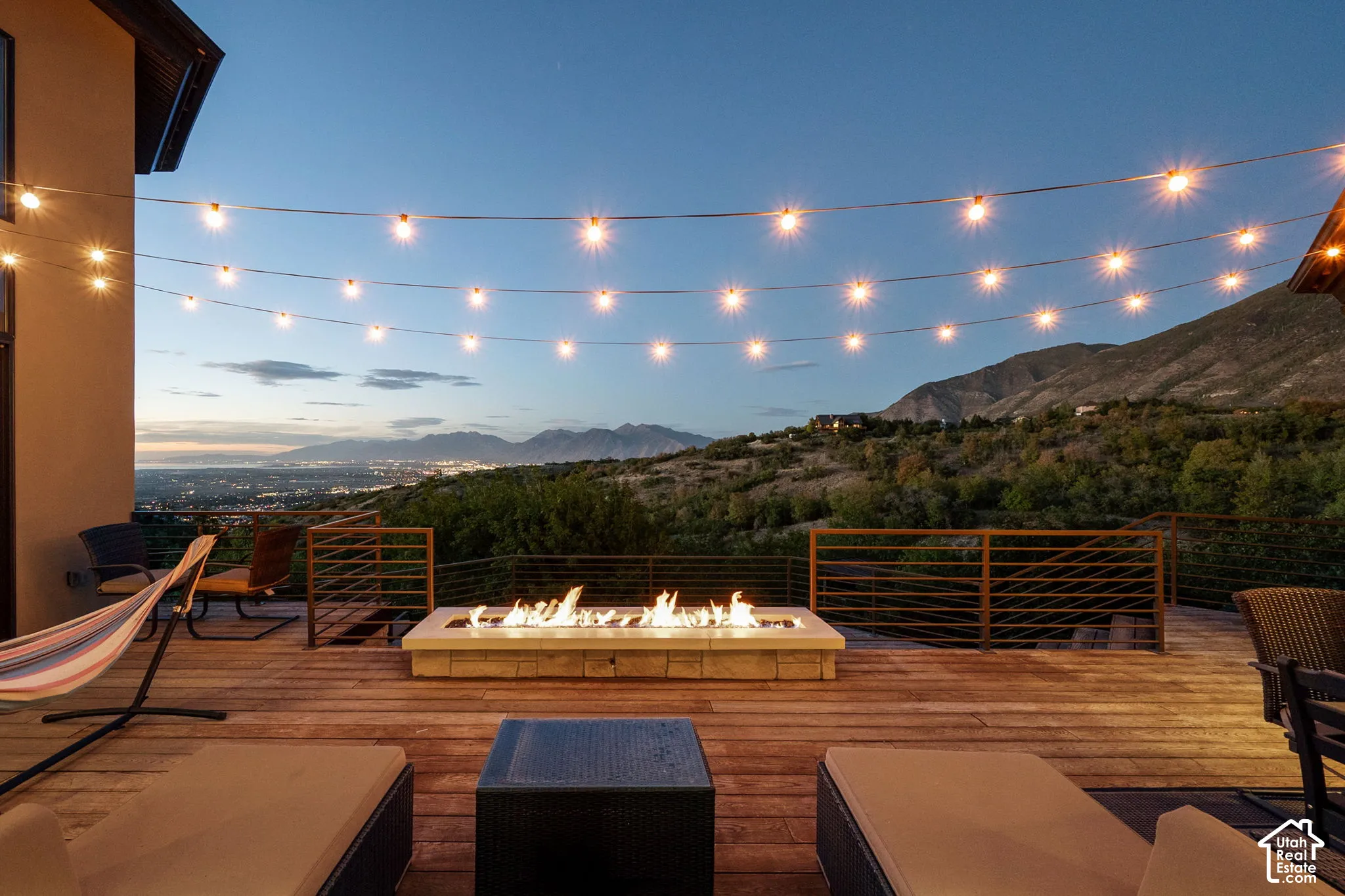 Expansive wood-finish deck with a built-in fire pit, string lighting, and metal railings