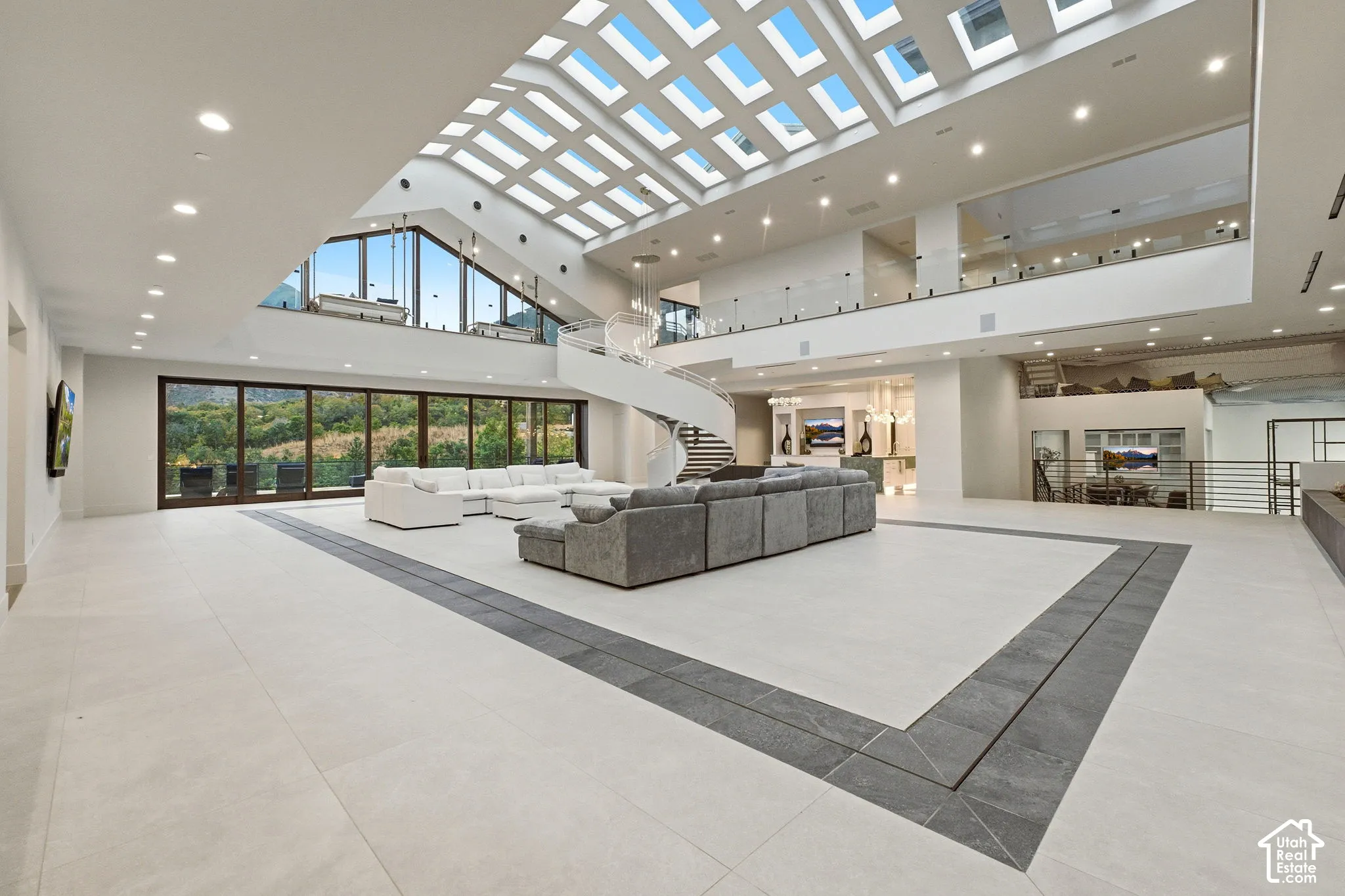Expansive great room featuring a coffered skylight, floor-to-ceiling glass doors, a spiral staircase, and light-toned tile flooring with a darker tile inlay