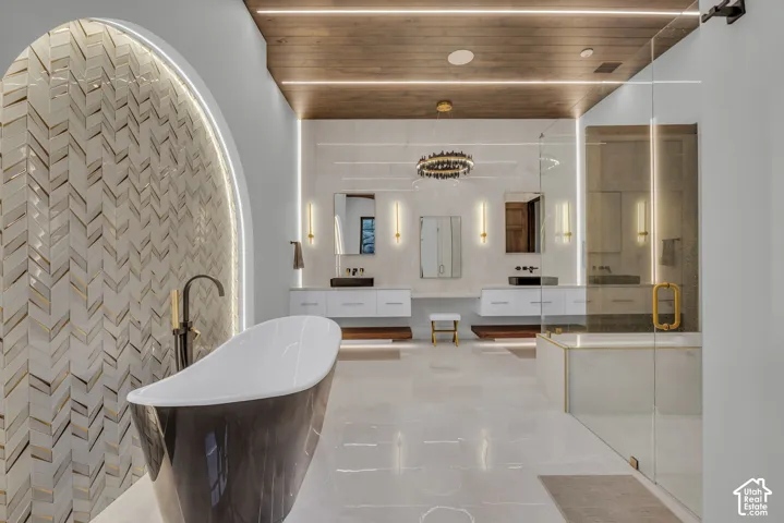 Freestanding soaking tub, arched chevron-patterned tile wall, dual floating vanities with vessel sinks, walk-in glass-enclosed shower, and wood-finish ceiling