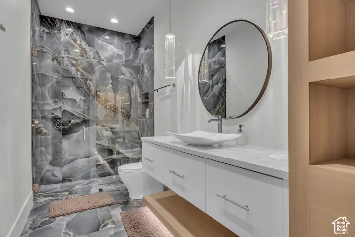 Glass-enclosed shower with large format stone-look tile, floating vanity with white vessel sink, rounded wall mirror, and integrated wood-finish shelving