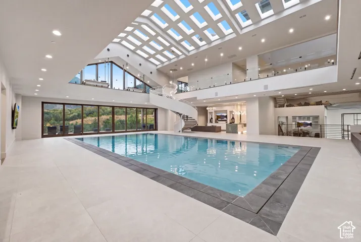 Indoor pool with light-toned tile surround, glass railings, spiral staircase, and expansive skylights