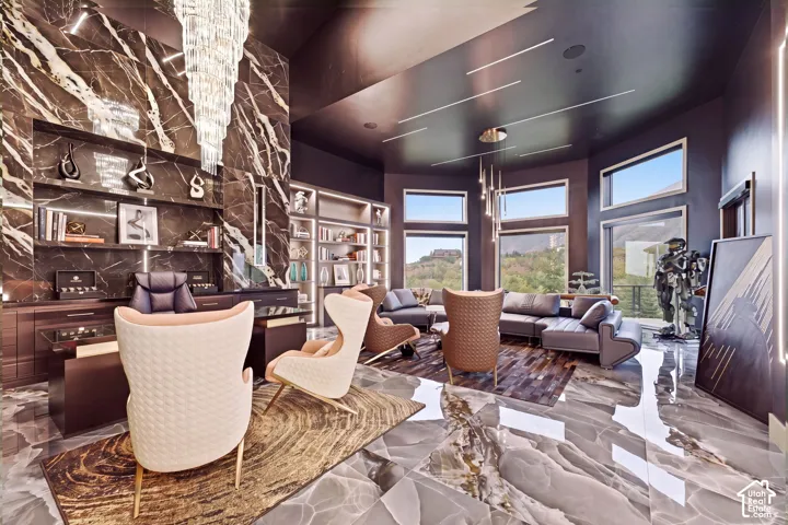 Polished stone flooring, floor-to-ceiling accent wall, built-in shelving, expansive windows, and a tiered chandelier