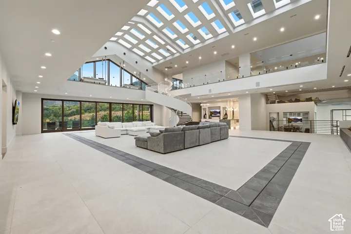 Expansive great room featuring a coffered skylight, floor-to-ceiling glass doors, a spiral staircase, and light-toned tile flooring with a darker tile inlay