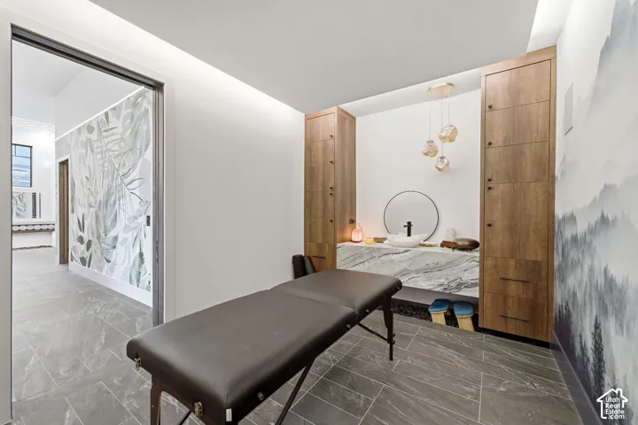 Recessed lighting, wood-finish built-in cabinetry, stone-finish flooring, wall-mounted vanity with vessel sink, and decorative wall coverings