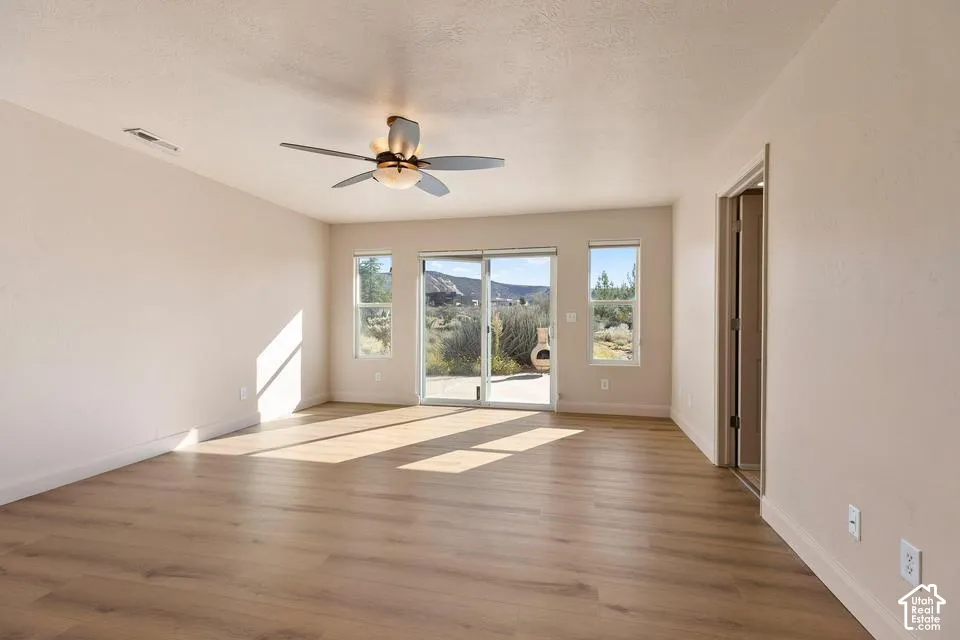 Wood-finish flooring, ceiling fan, sliding glass door, multiple windows, and a doorway with a mirrored surface