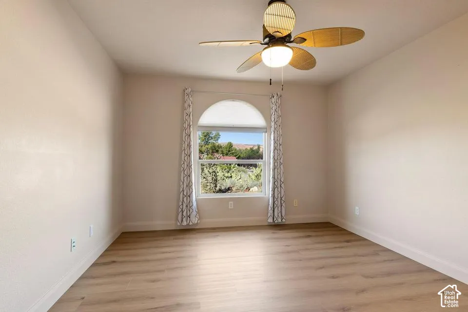 Bright, light-filled bedroom showcasing wood-finish flooring, neutral walls, and a ceiling fan with integrated lighting