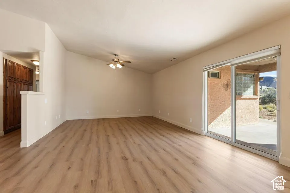 Wood-finish flooring throughout, vaulted ceiling, ceiling fan, sliding glass door to an outdoor patio, and built-in wood cabinetry