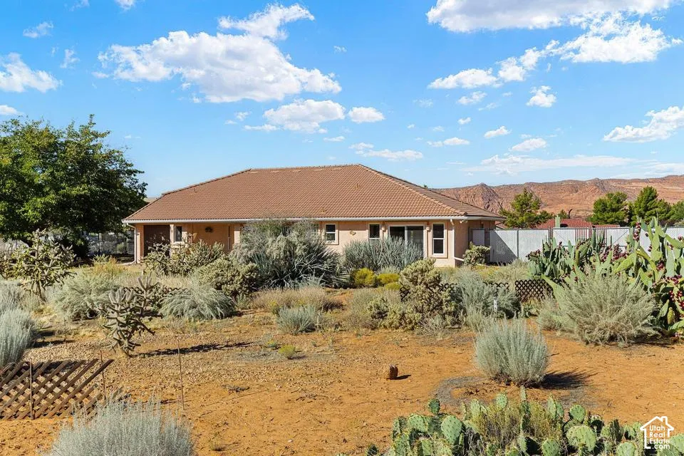 Desert landscaping with various cacti and brush, tan stucco exterior, tiled roofing, and a privacy fence
