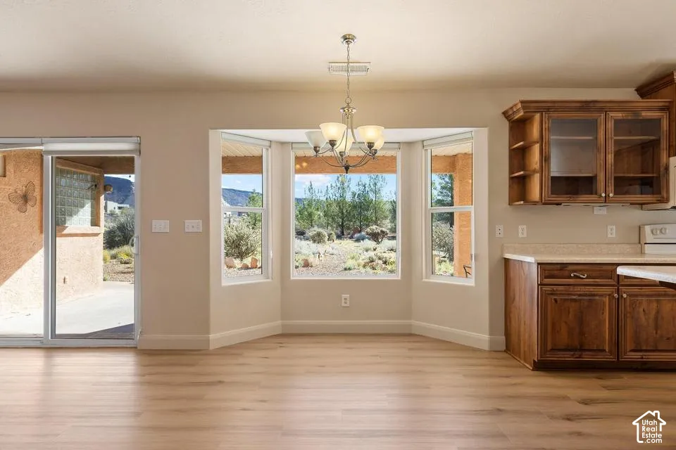 Bay window with multiple panes, wood-finish flooring, kitchen cabinetry with glass-front uppers, sliding glass door, and a traditional chandelier