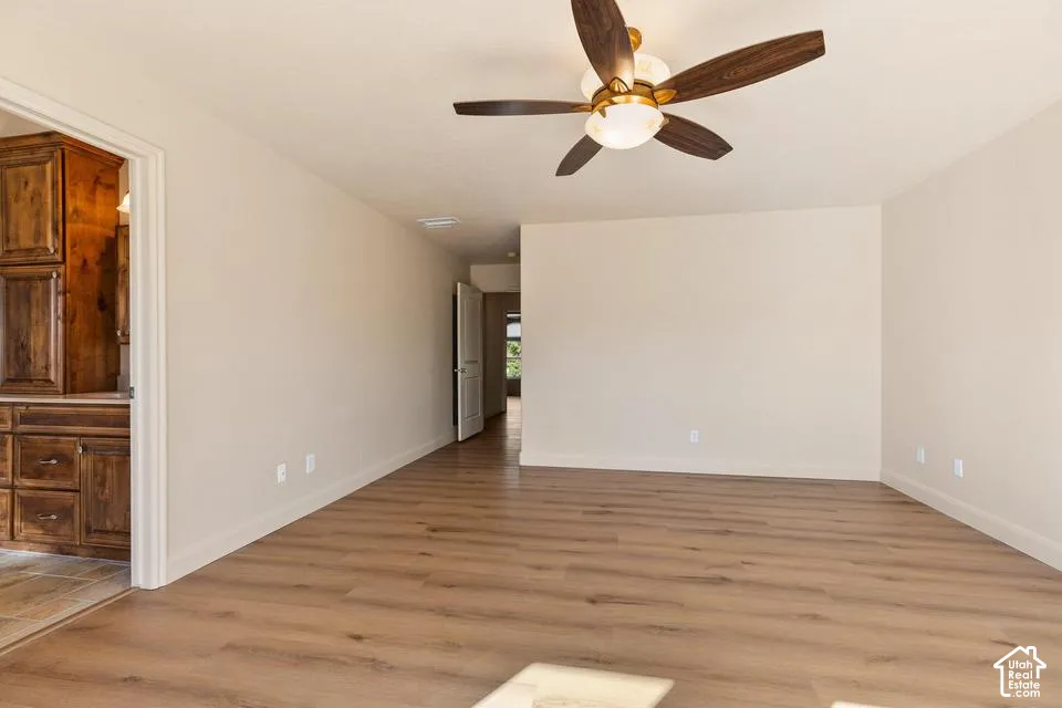 Spacious room featuring wood-finish flooring, light-toned walls, and a ceiling fan with integrated lighting
