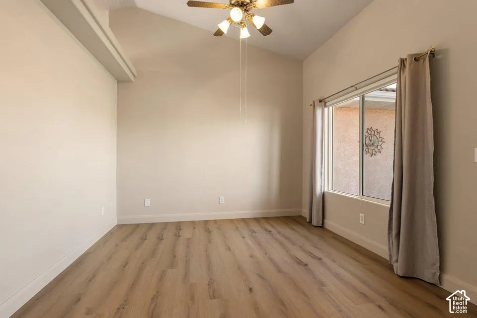 Vaulted ceiling with a ceiling fan light fixture, wood-finish flooring, and a large window