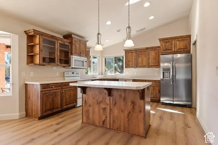 Chef's kitchen featuring custom wood cabinetry with glass-front upper cabinets, a large center island with wood-finish base and white countertop, stainless steel appliances including a side-by-side refrigerator, pendant lighting, recessed ceiling lights,
