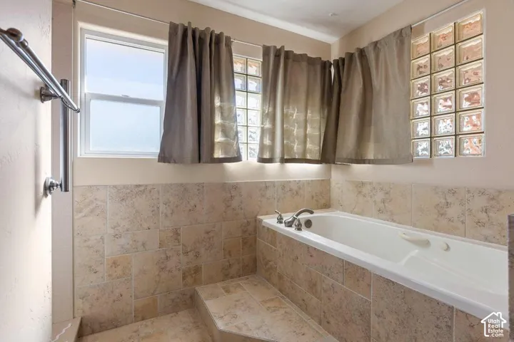 Built-in soaking tub with chrome fixtures, surrounded by neutral-toned tile