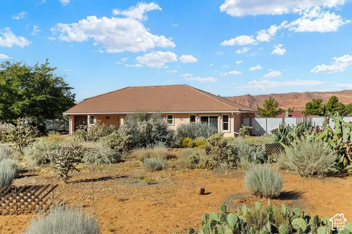 Desert landscaping with various cacti and brush, tan stucco exterior, tiled roofing, and a privacy fence
