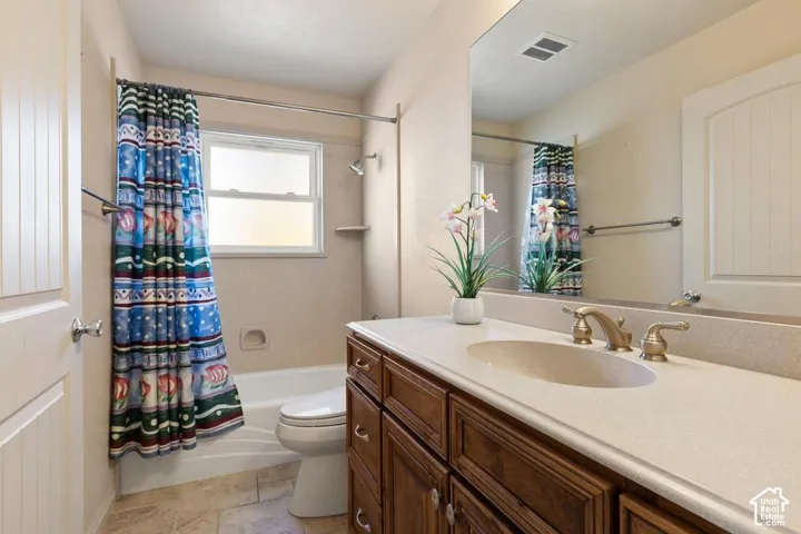 Bathroom featuring a single window, a built-in shower/tub combination, a vanity with a counter-mounted sink, and a large wall-mounted mirror
