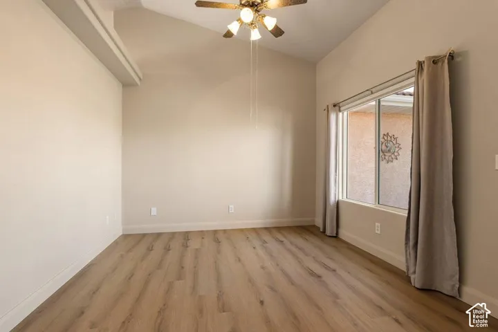 Vaulted ceiling with a ceiling fan light fixture, wood-finish flooring, and a large window