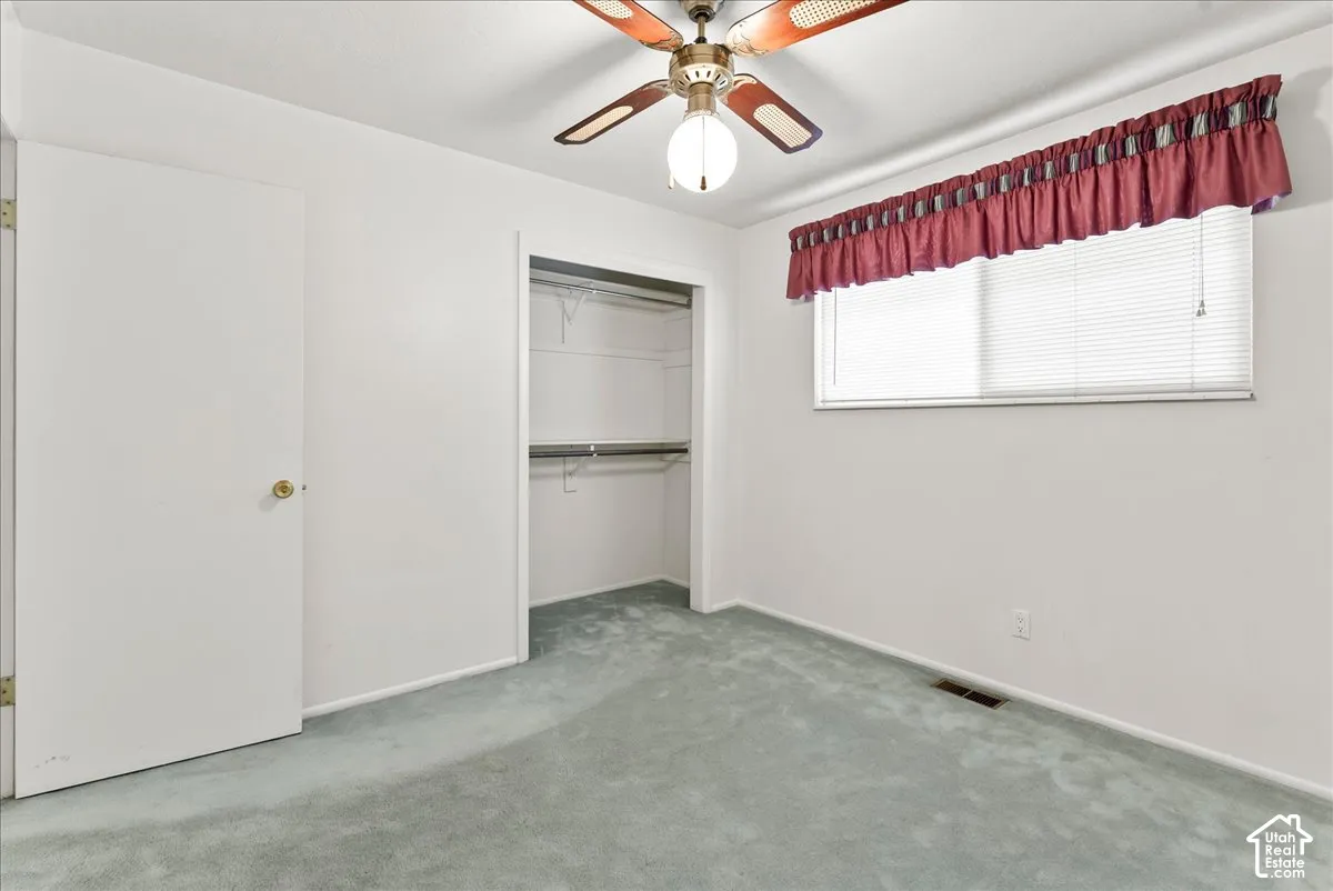 Recessed closet with built-in shelving, ceiling fan with integrated lighting, window with blinds, and light blue carpeting