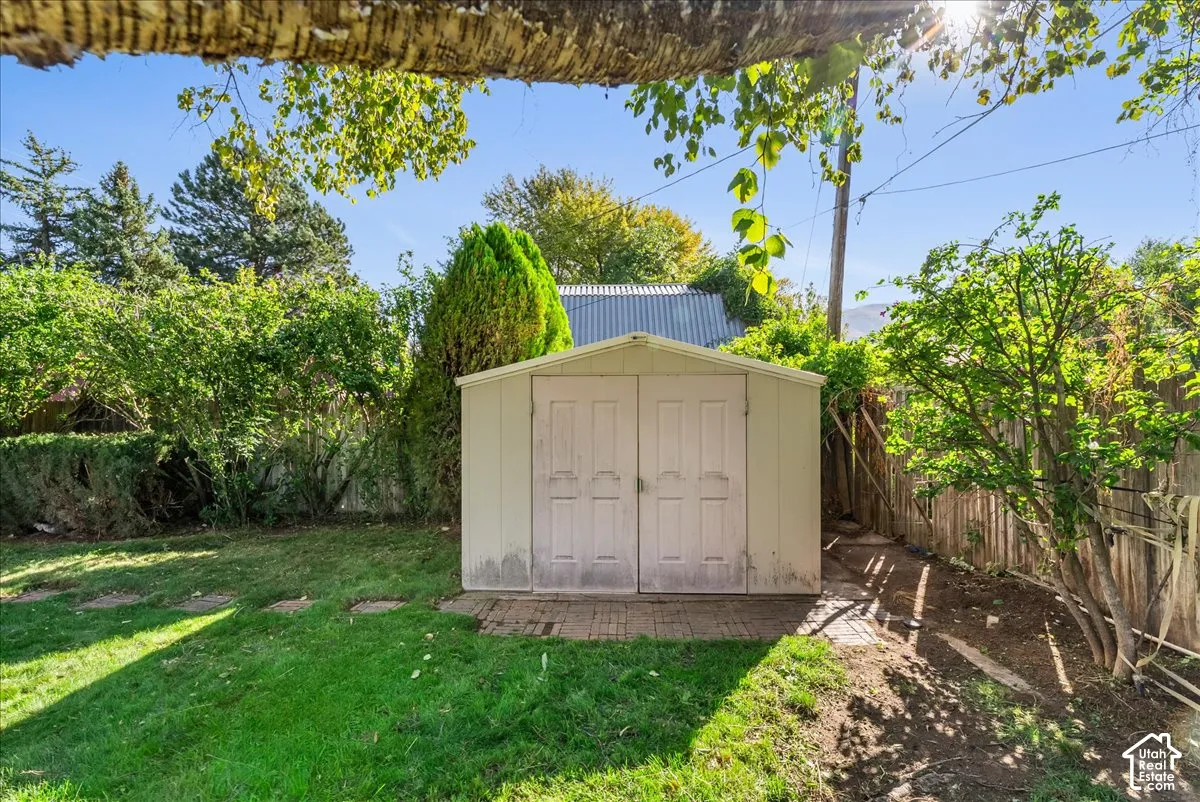 Expansive backyard featuring a manicured lawn, established perimeter landscaping, and a utility shed with double doors on a brick paver foundation