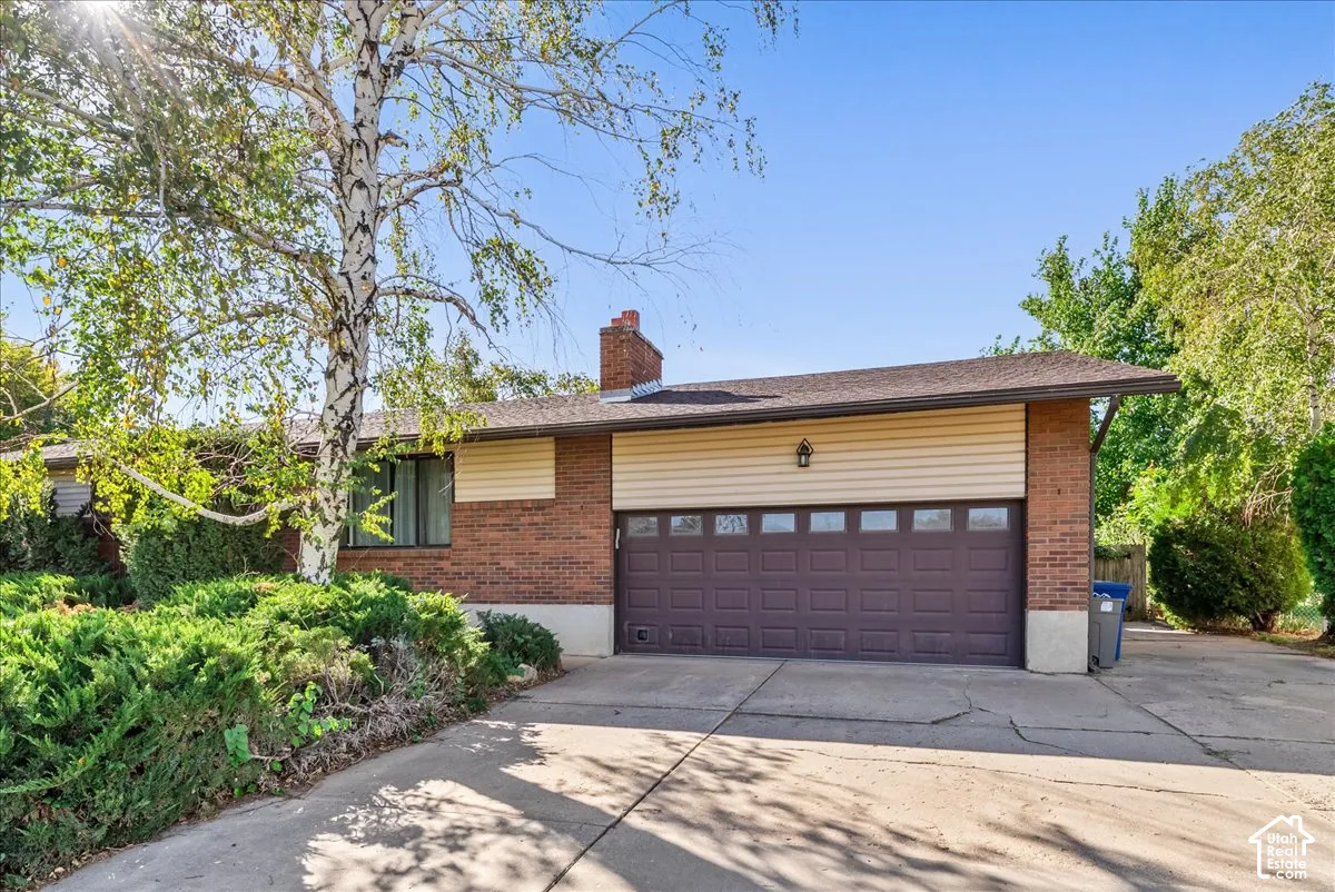 Brick and siding exterior with an attached garage, paved driveway, and mature landscaping