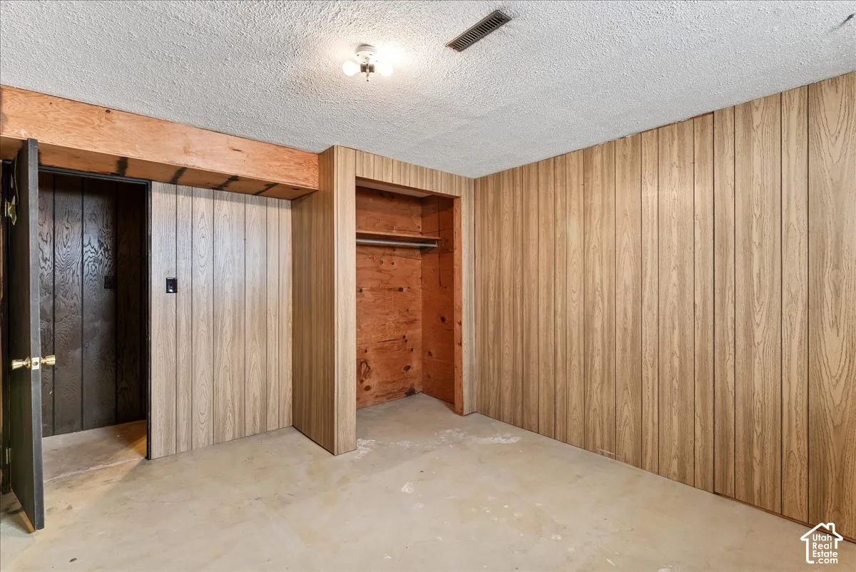 Wood-finish wall paneling, built-in closet with hanging rod, exposed wood beam, concrete flooring, and ceiling-mounted light fixture